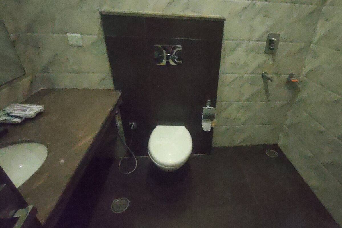 A small, dimly lit bathroom with a white toilet, a dark door, and a tiled wall.