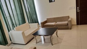 A living room with a white sofa, a beige sofa, and a black coffee table. - Eden Green (Ganaur)