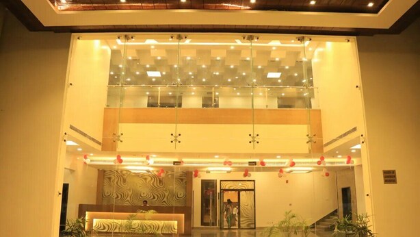 A hotel lobby with a reception desk, glass walls, and a staircase. - Eden Green (Ganaur)