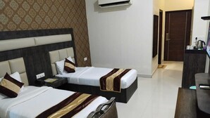 A hotel room with two beds, a desk, a chair, and an air conditioning unit. - Eden Green (Ganaur)