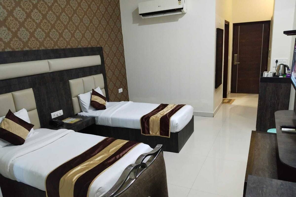 A hotel room with two beds, a desk, a chair, and an air conditioning unit.