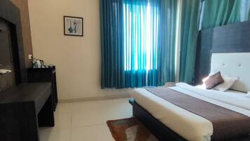A hotel room with a large bed, a TV mounted on the wall, a bedside table, and a window with curtains.