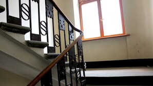 Una scala con ringhiere in metallo decorate e corrimano in legno, che conduce a un pianerottolo con una finestra sopra.
