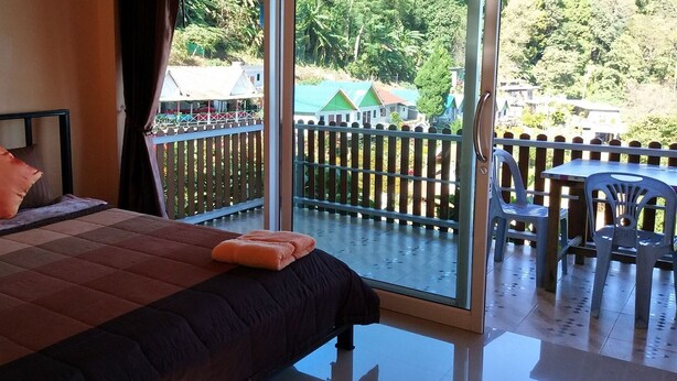 Un dormitorio con cama, almohadas y vistas a un balcón con barandilla y mesa.