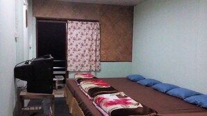 Una habitación estrecha con una cama larga, un escritorio con computadora y una ventana con cortinas.