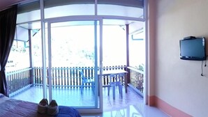 Una habitación con una cama, una mesita con botellas, un televisor y un balcón con barandilla.