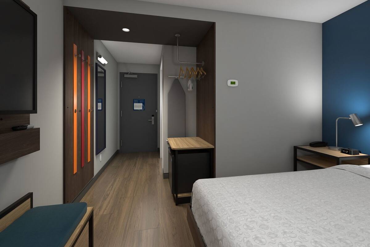 A hotel room with a bed, bedside table, TV, and a desk with a chair.