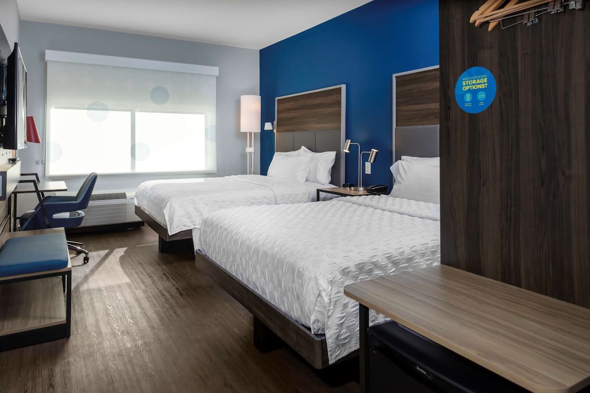 A hotel room with two beds, a desk, a chair, and a TV.