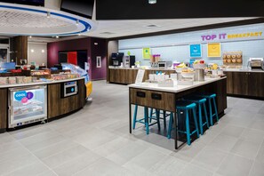 A modern breakfast area with a counter displaying various food items, a refrigerated display, and a seating area with stools.