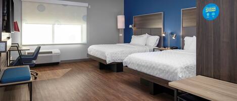A hotel room with two beds, a desk, a chair, a TV, and a window with blinds.