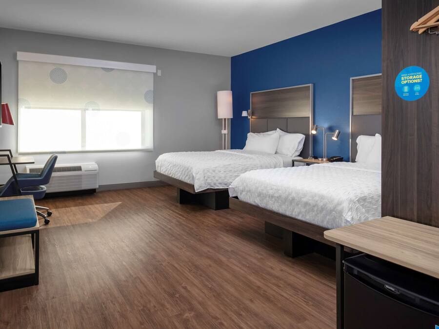 A hotel room with two beds, a desk, a chair, a TV, and a window with blinds.