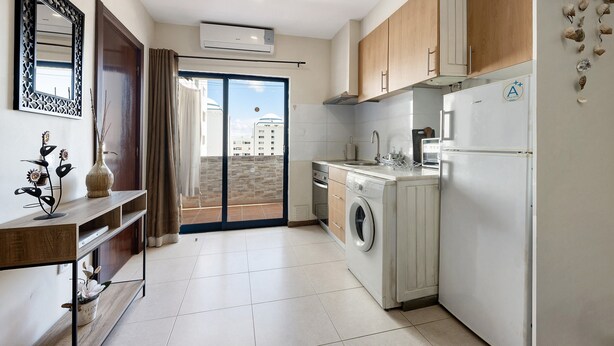 A modern kitchen with a washing machine, a built-in oven, and a refrigerator. - Holiday Apartment “Da Praia” with Air Conditioning, Balcony, Shared Garden & WiFi (Portimão)