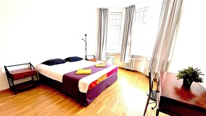 A bedroom with a bed, bedside table, and a desk with a plant.