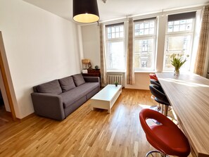 A modern living room with a grey sofa, a white coffee table, and a wooden dining table with red chairs.