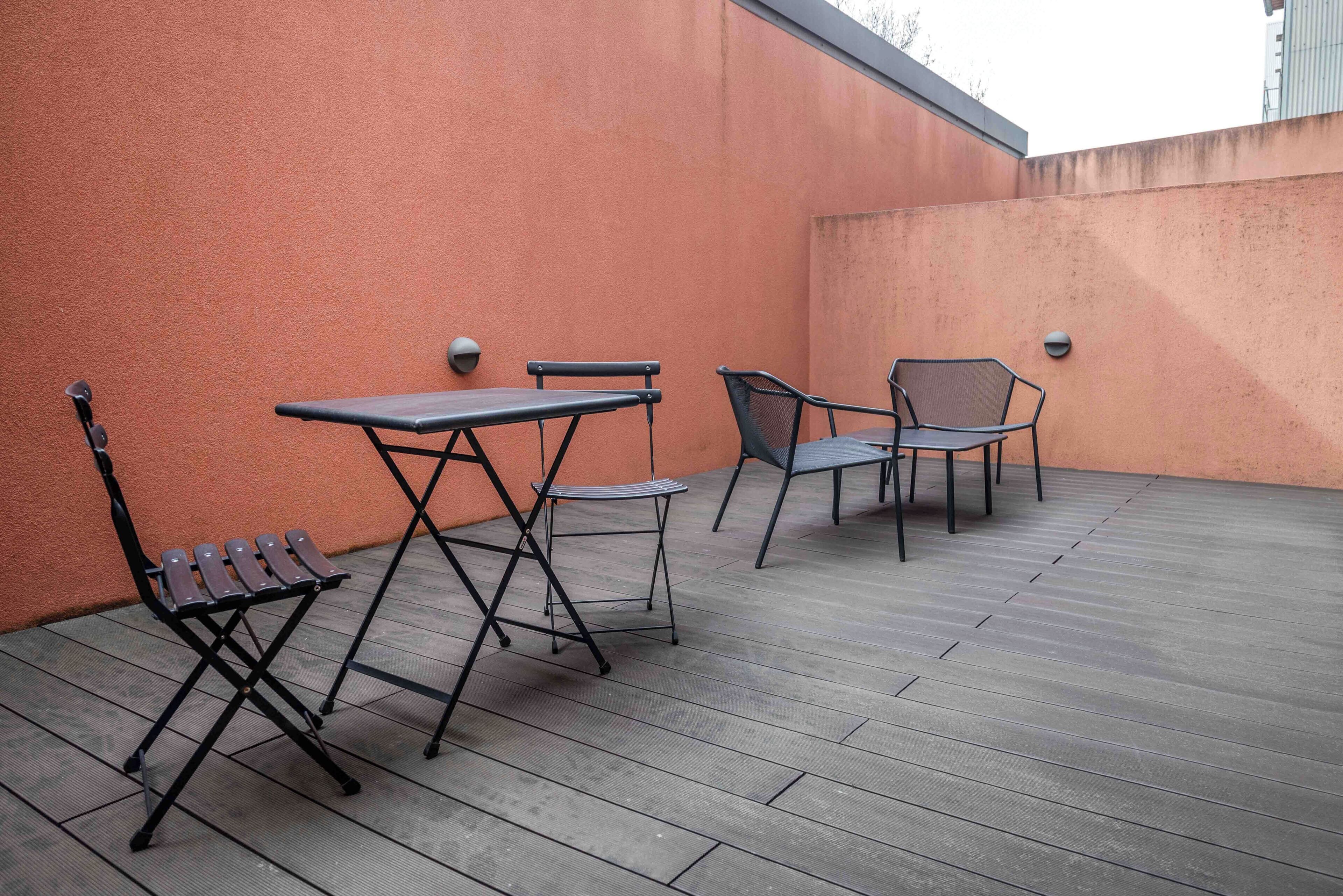 An outdoor patio with a wooden deck, a table, two chairs, and a small stool.