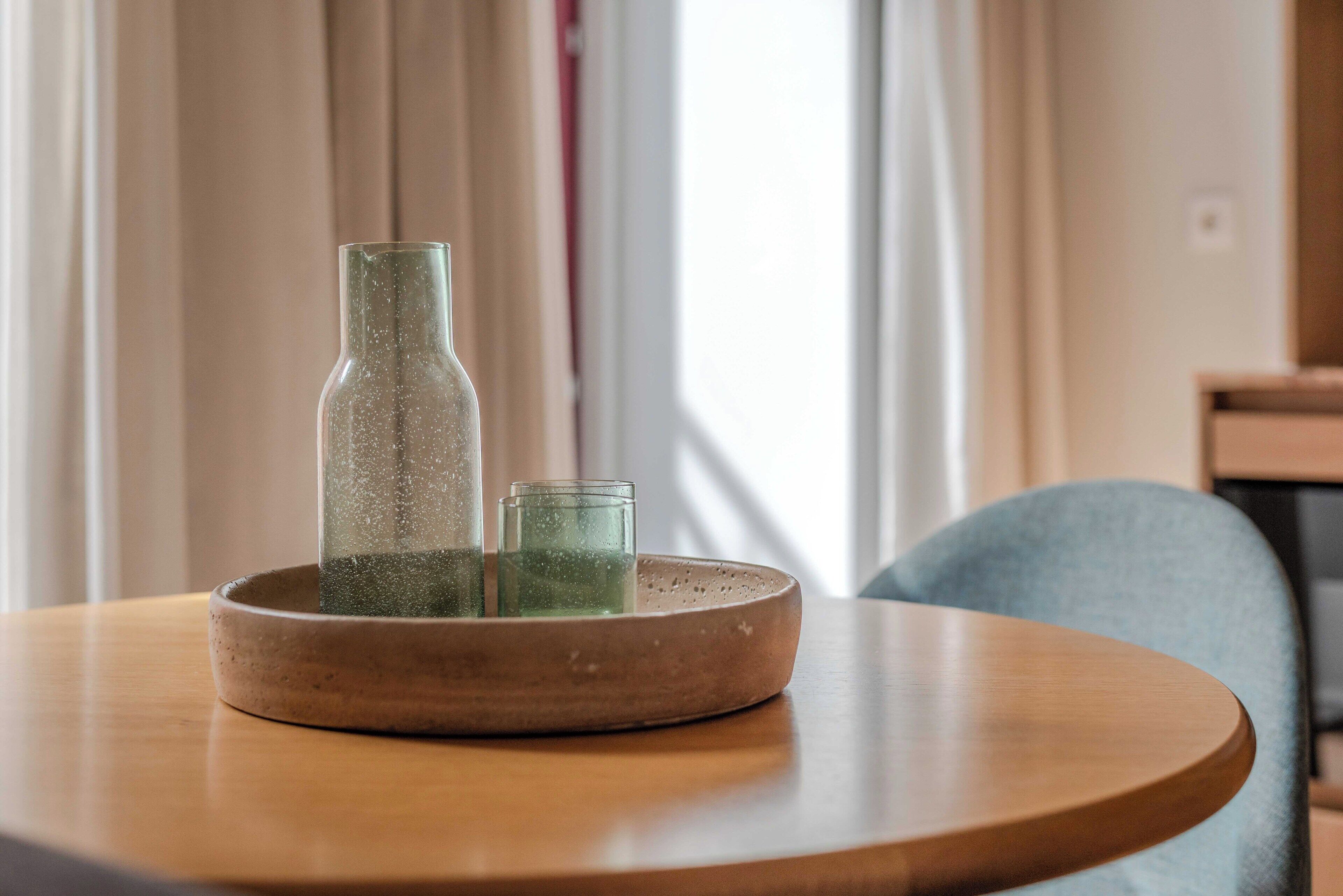 Une table ronde en bois sur laquelle repose un plateau en céramique, lui-même supportant deux bouteilles en verre et un verre.
