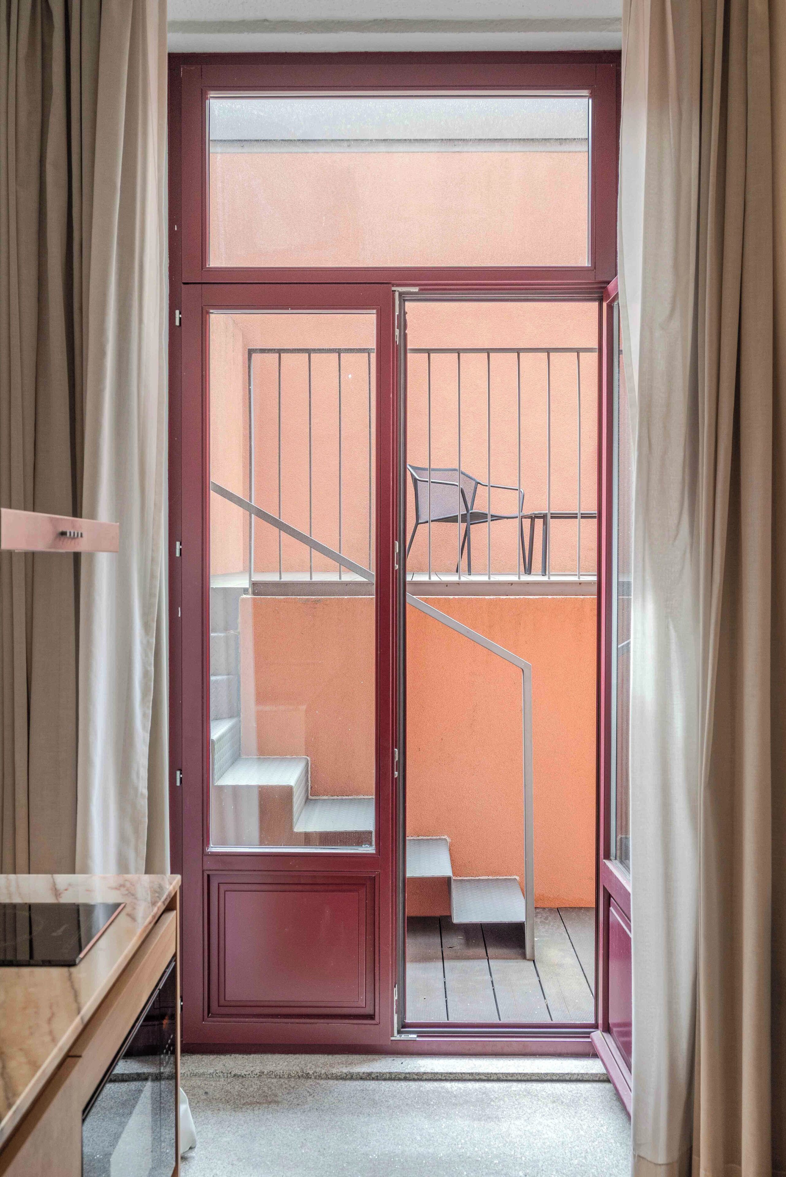 A room with a sliding glass door leading to a balcony with a metal railing and a chair.