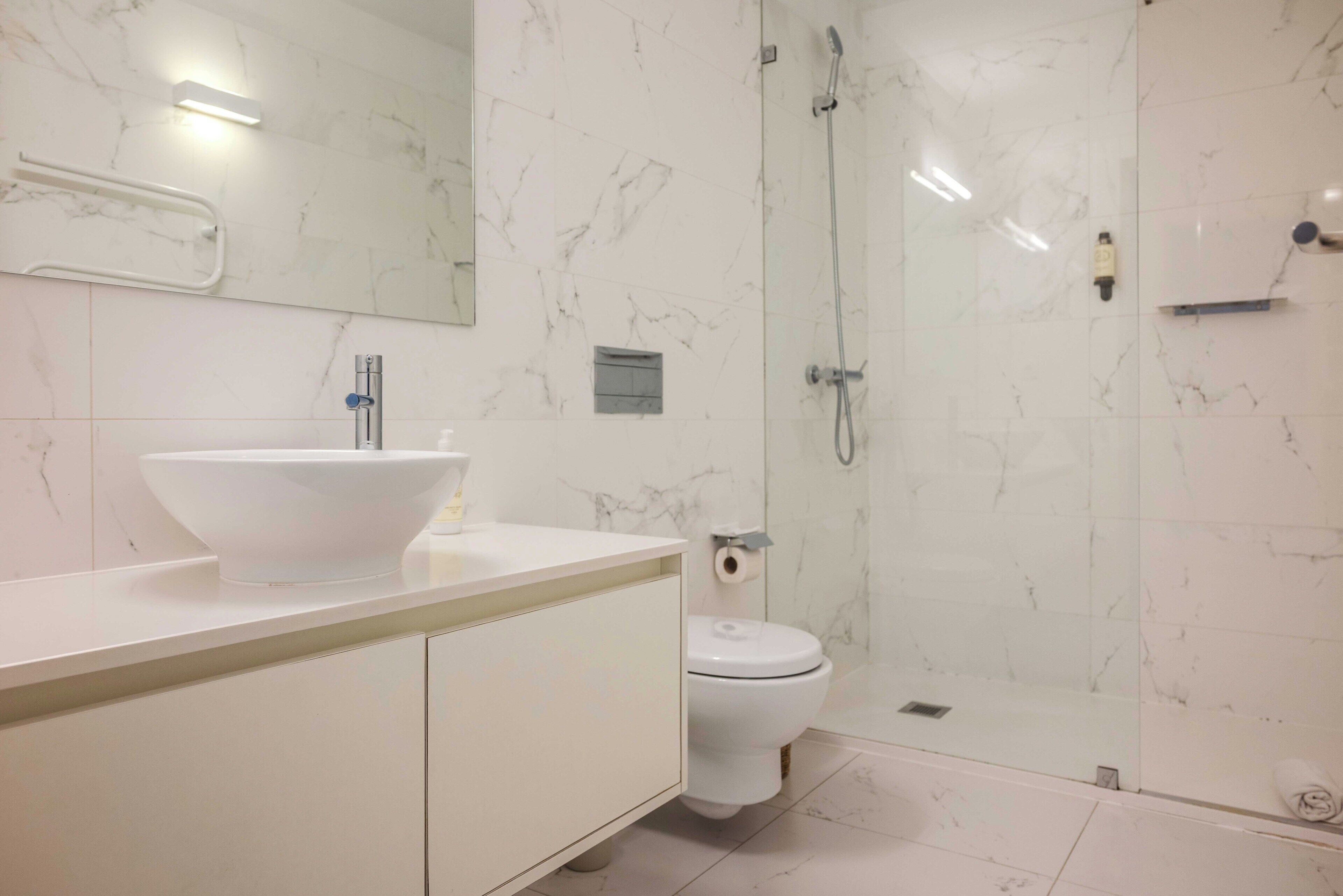 A modern bathroom with a white marble sink, a toilet, and a glass-enclosed shower.