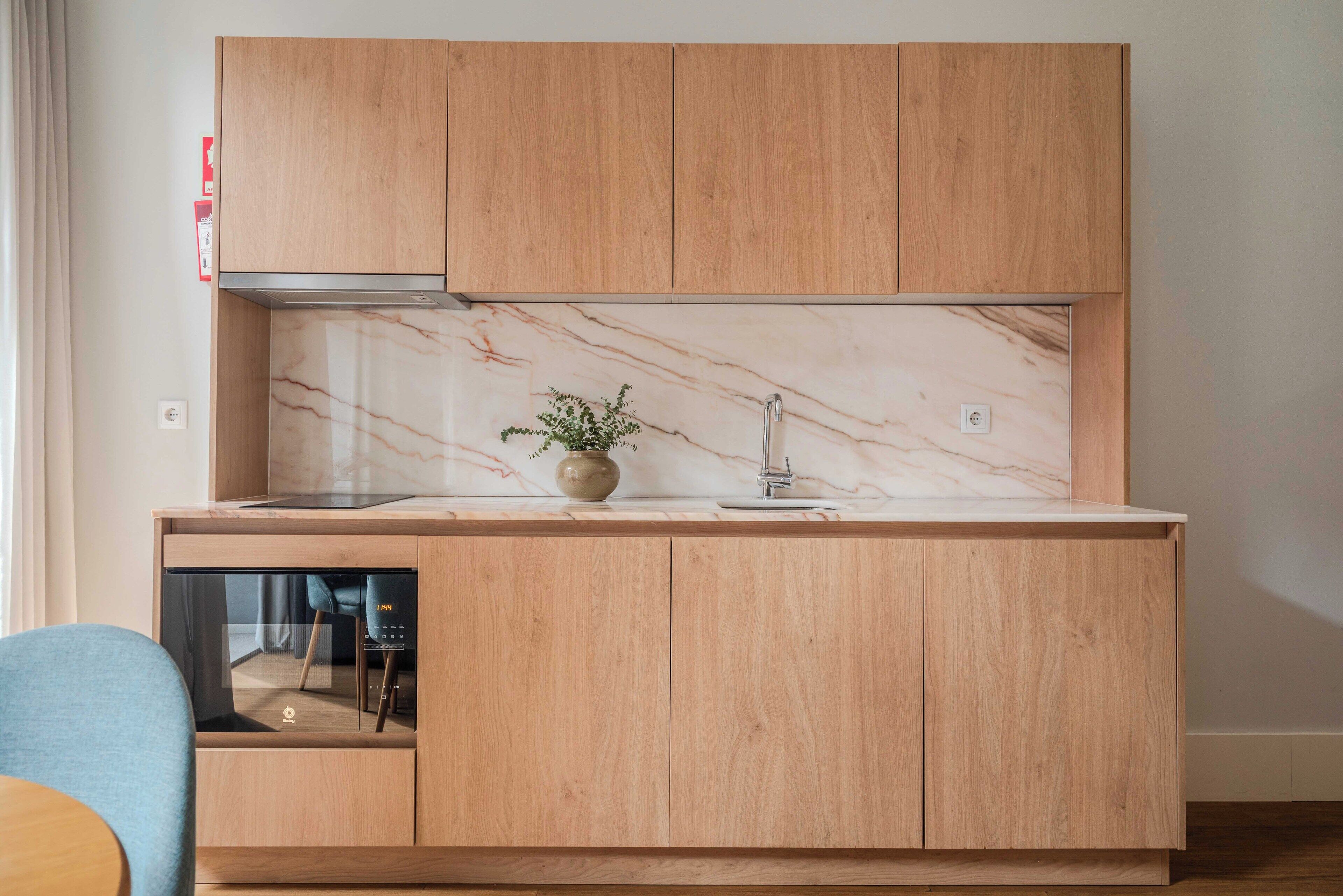 A modern kitchen with wooden cabinets, a marble backsplash, and a built-in oven.