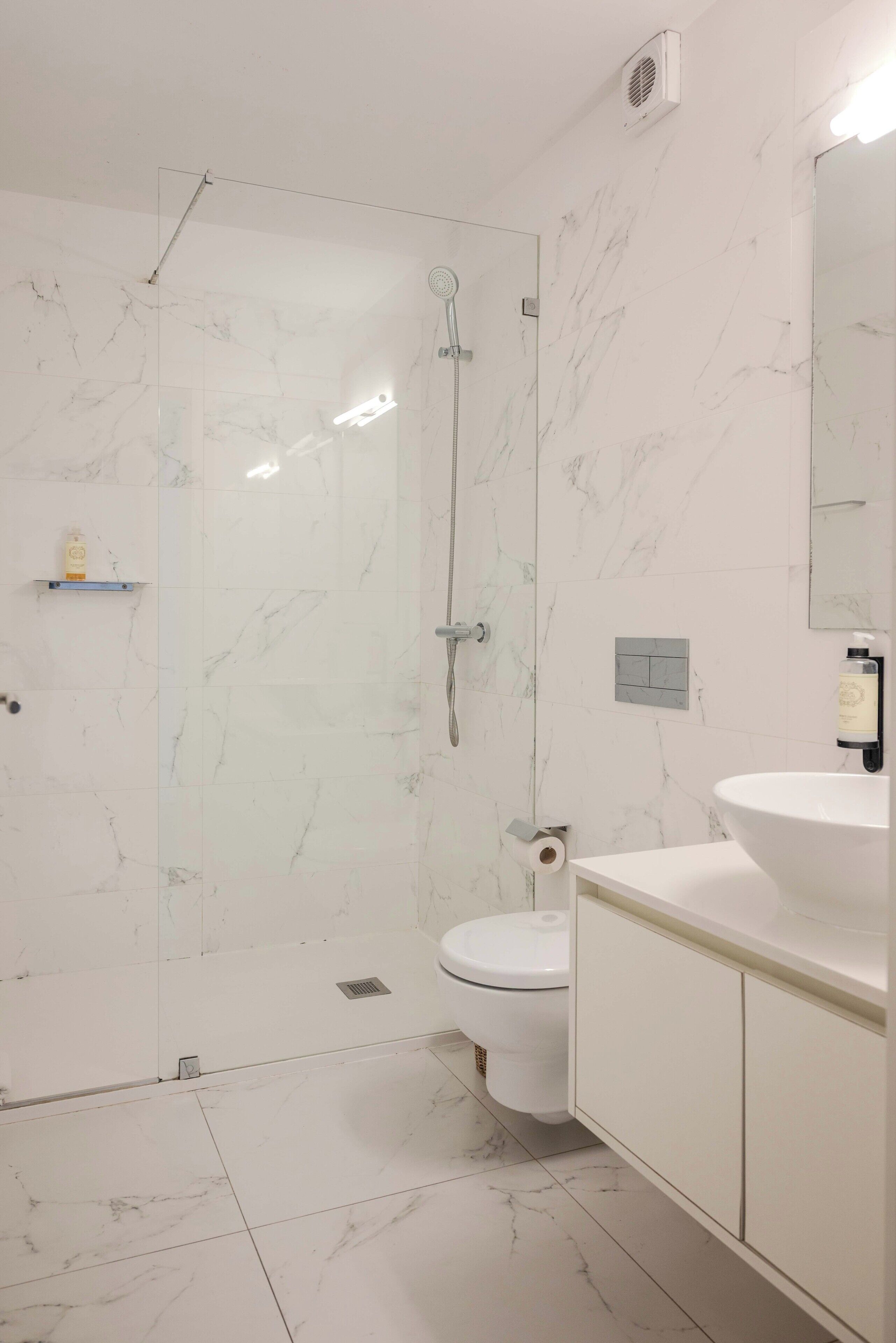 A modern bathroom with a glass-enclosed shower, a toilet, and a sink with a mirror.