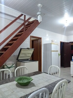 Simple, well-lit room with a wooden staircase and a dining area featuring a table and chairs.