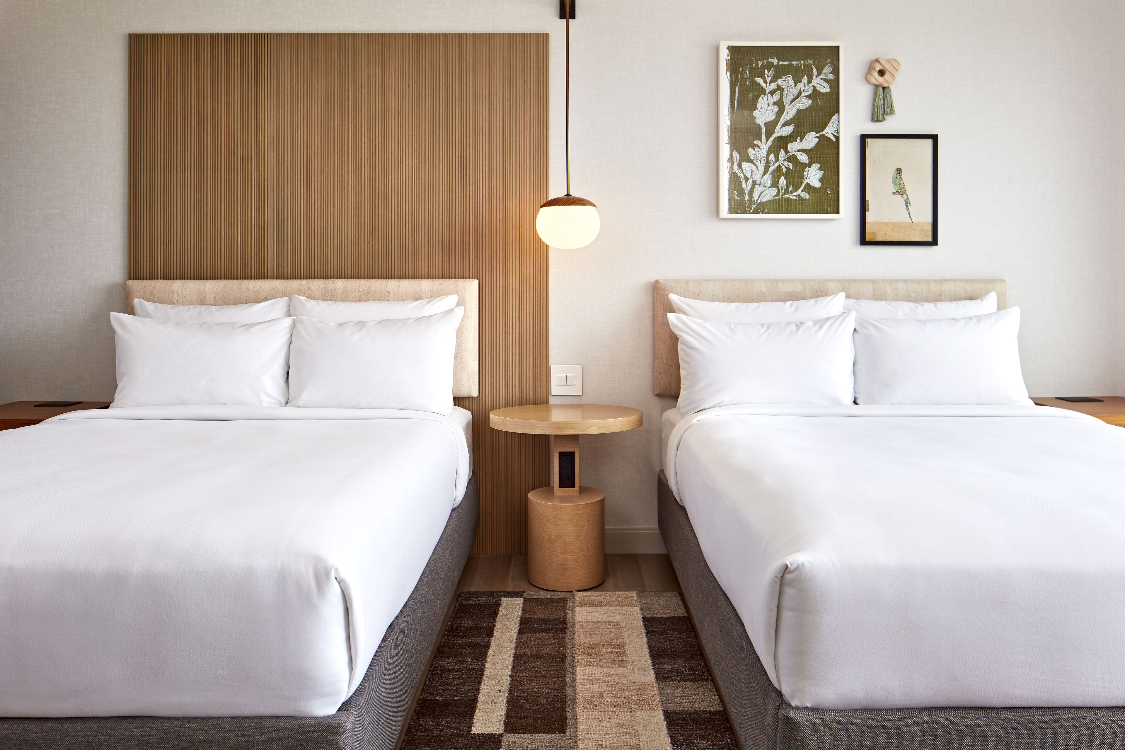 A hotel room with two beds, a wooden headboard, a small round table, and a hanging light fixture.