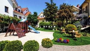 Un terrain de jeux avec un toboggan et un mur d ’escalade, entouré d’arbustes soigneusement taillés et d’un petit jardin.