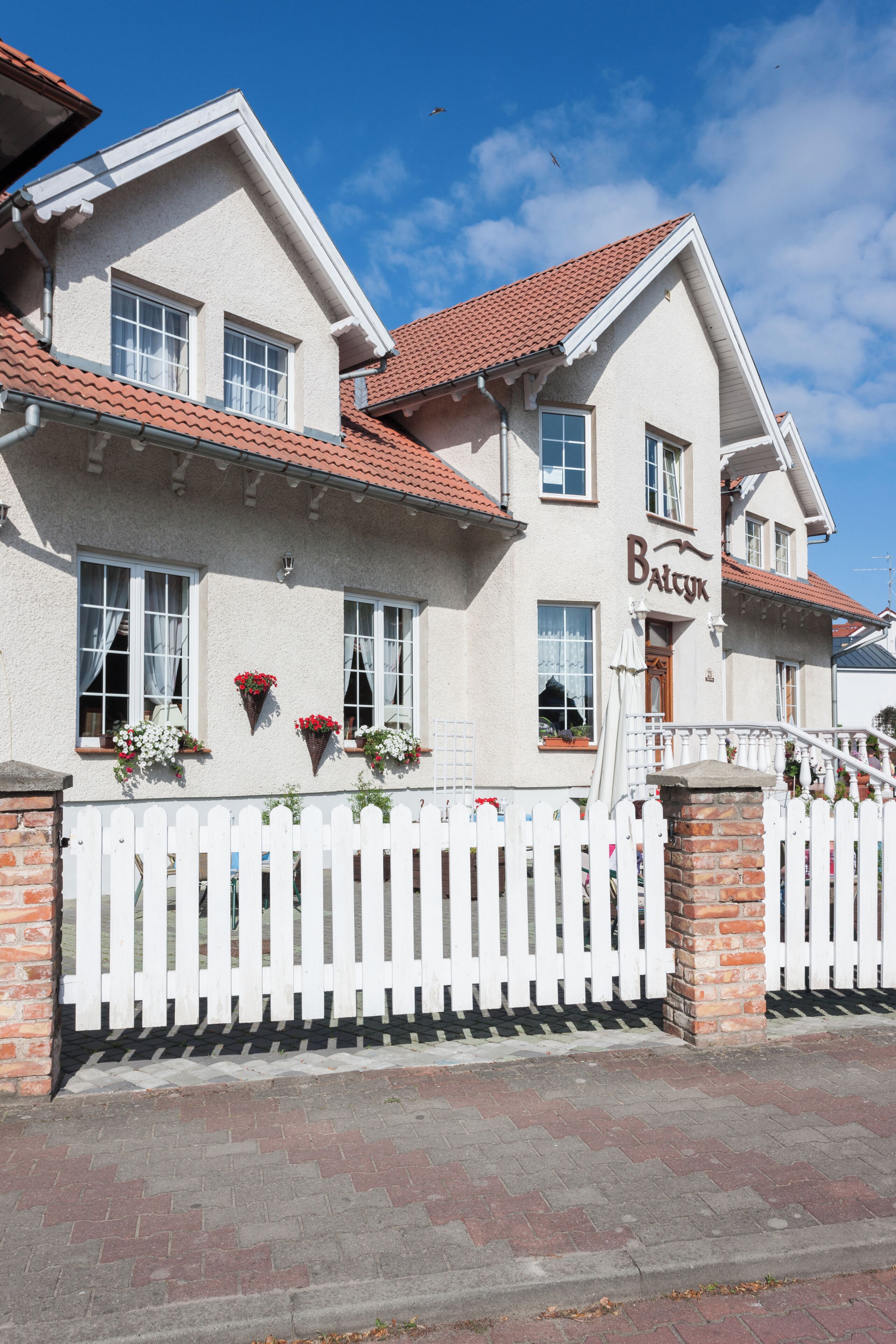 A two-story building with a white picket fence, a red-tiled roof, and a sign that reads 'Balck'.