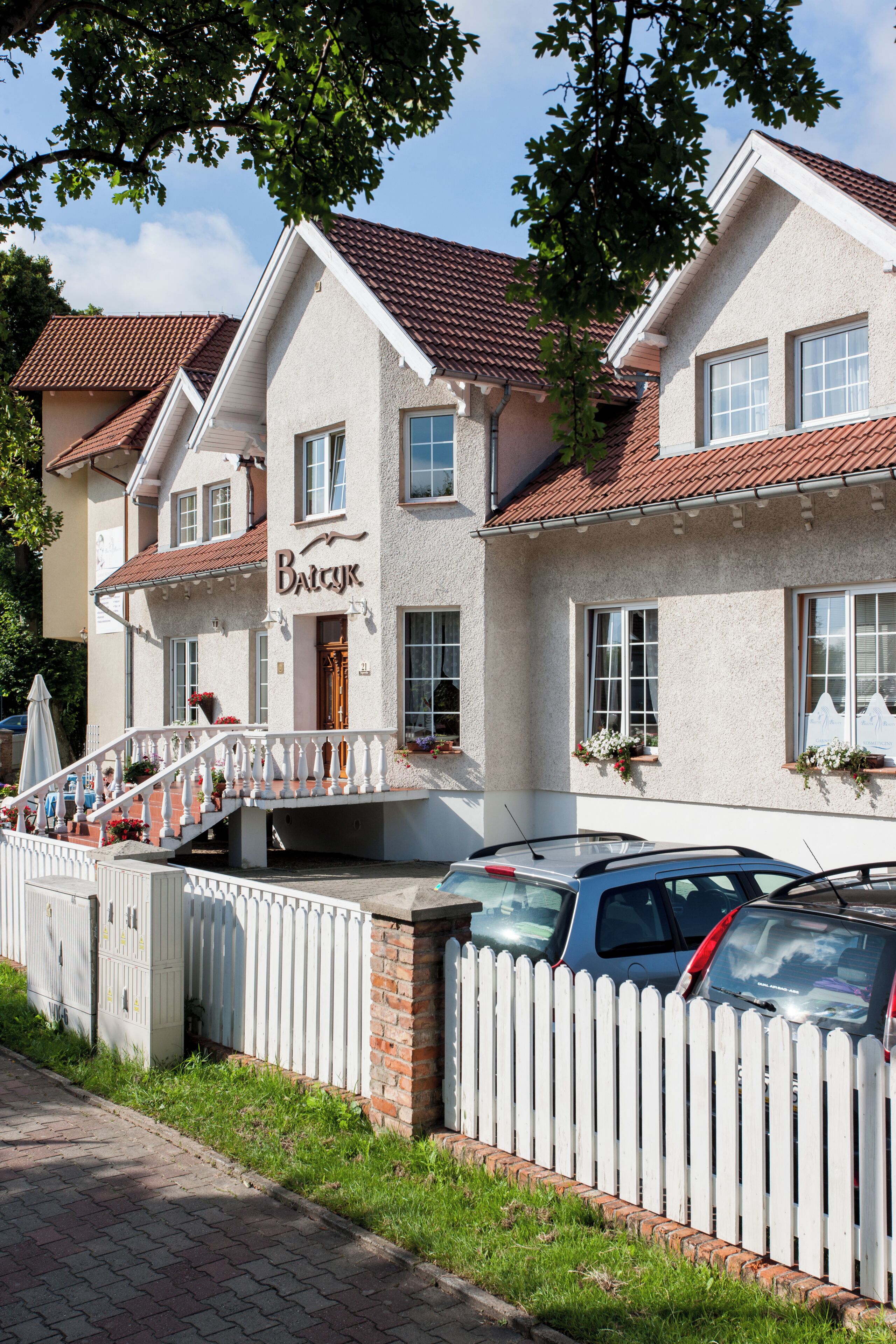 A two-story building with a white picket fence, a red-tiled roof, and a sign that reads 'Baczyk.'