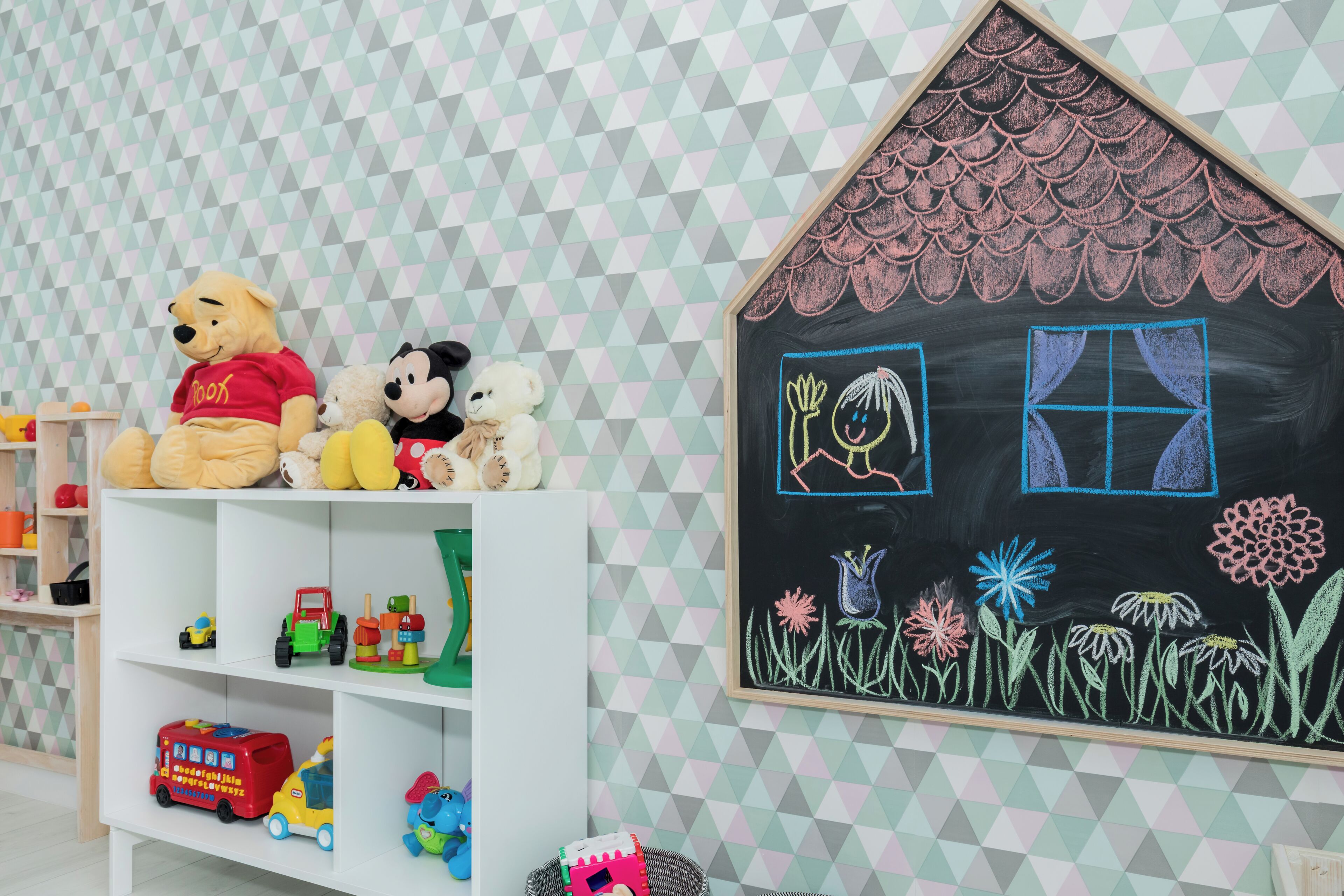 A children's play area with toys, a chalkboard with drawings, and a geometric-patterned wall.