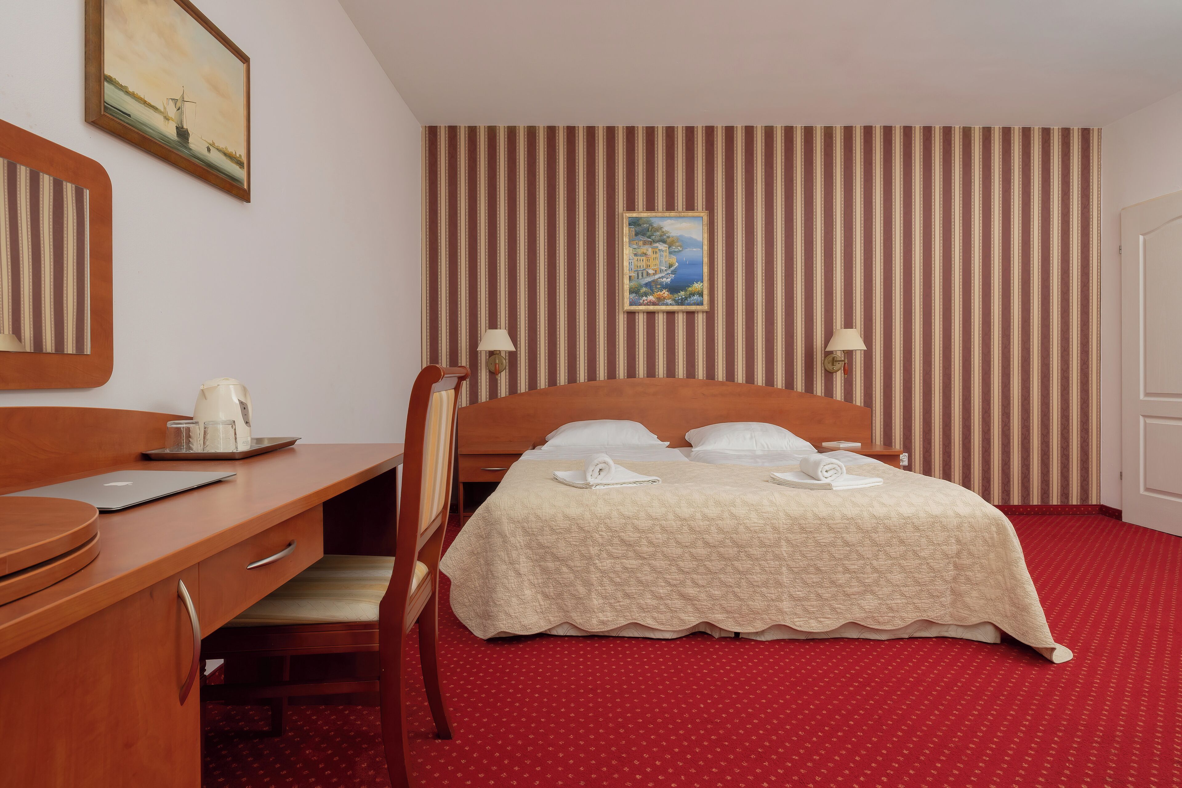 Ein Hotelzimmer mit Bett, Schreibtisch, Stuhl, Lampe und einem Bild an der Wand.