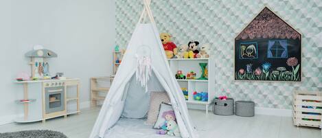 A playroom with a teepee, toys, and a wall painting.