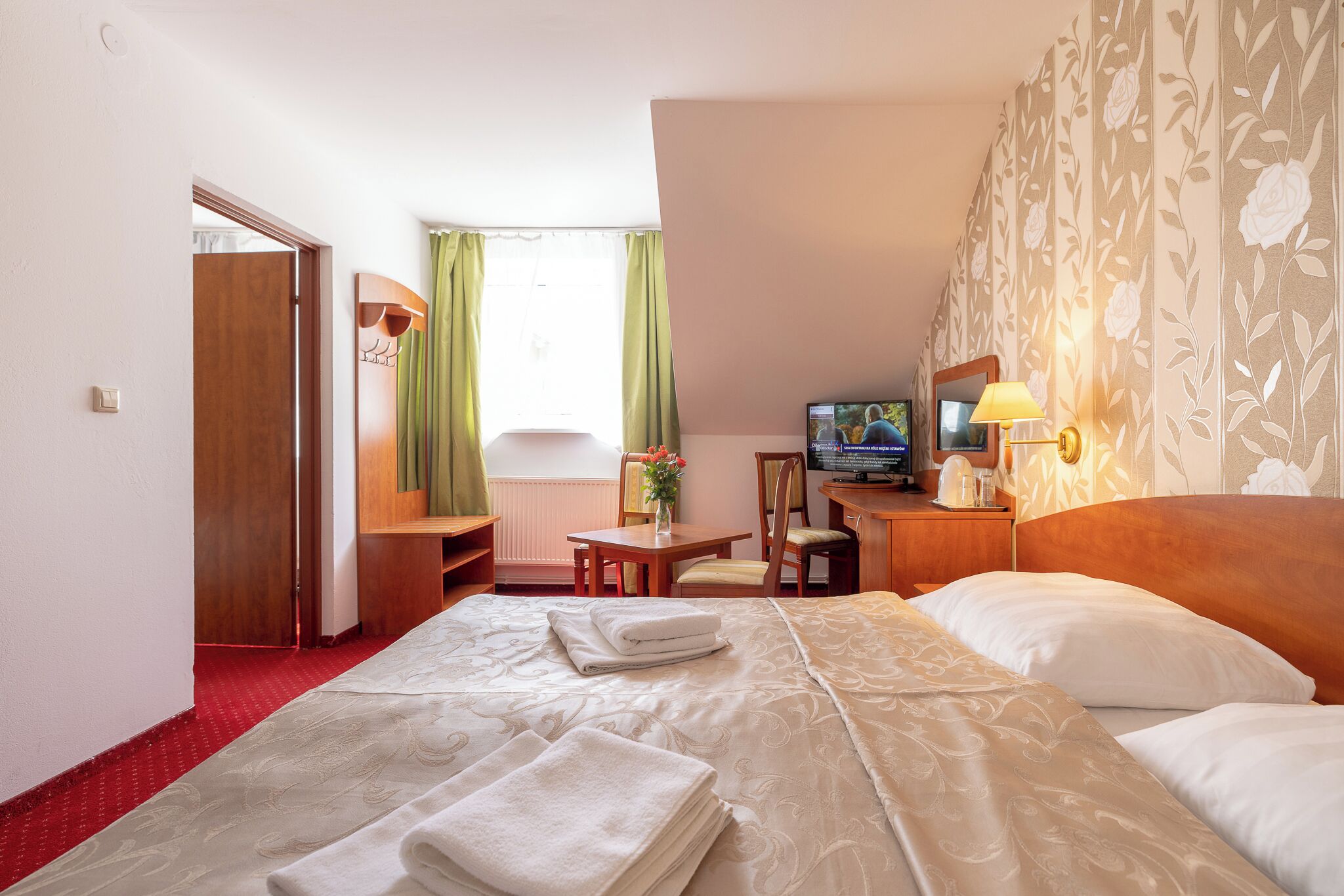 A hotel room with a bed, a desk, a chair, a television, and a window with curtains.