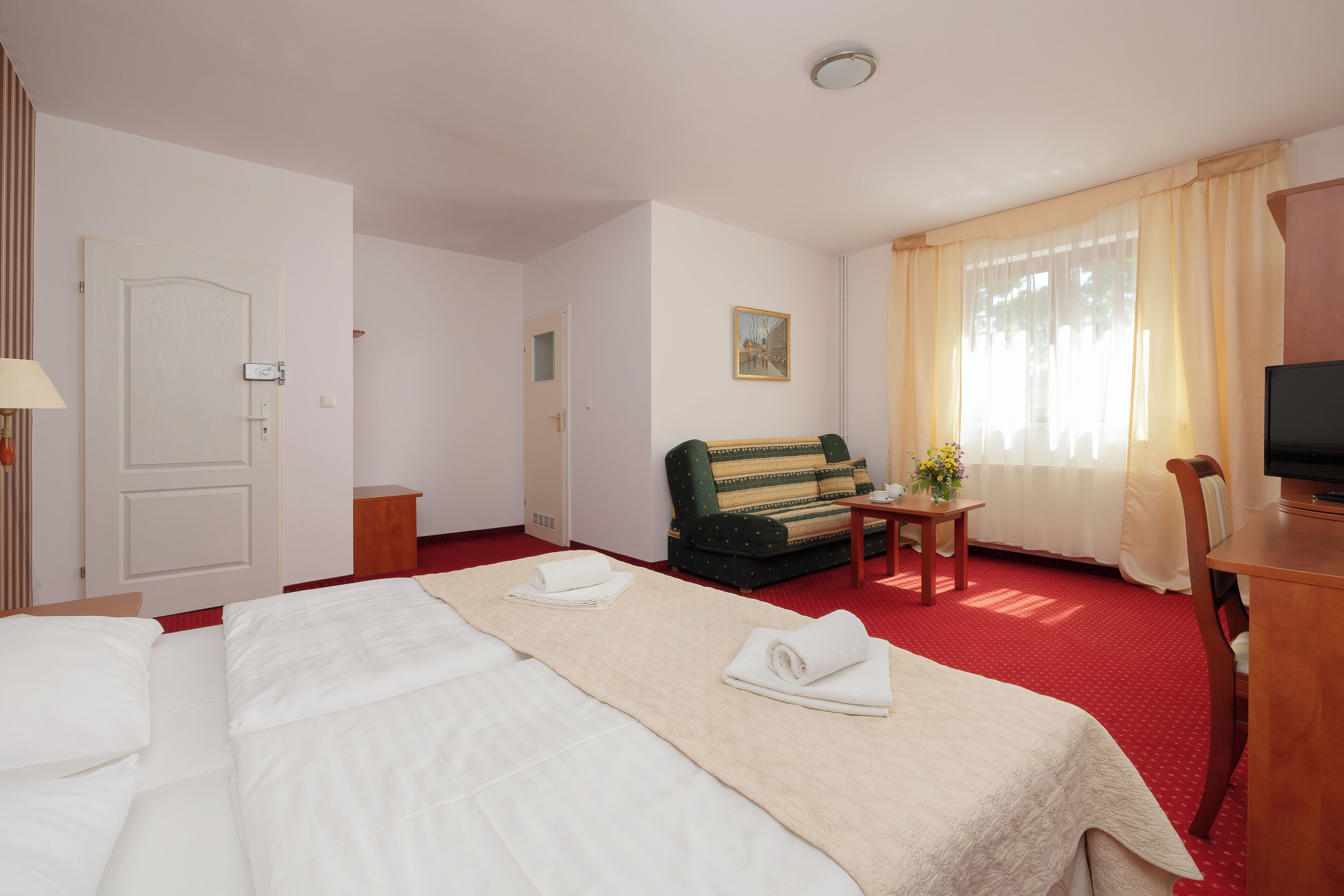 A hotel room with a large bed, a sofa, a TV, and a small table with a vase of flowers.