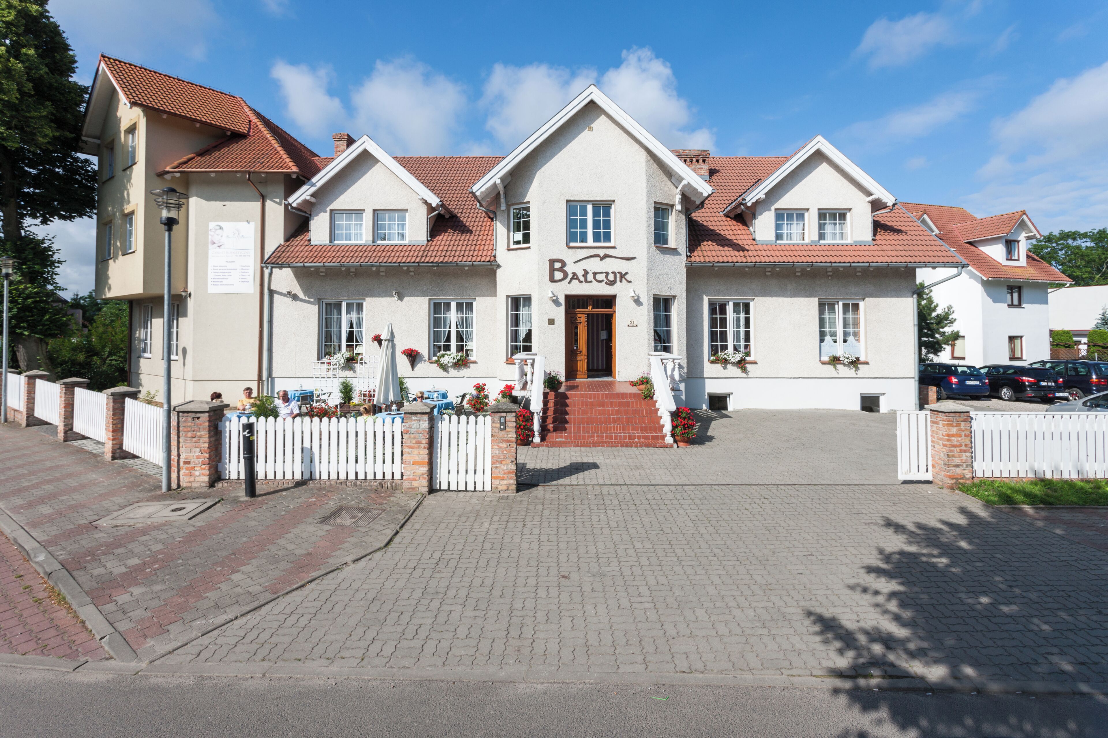 A two-story building with a sign reading 'Batyuk' at the entrance, a brick pathway leading to the door, and a white picket fence.
