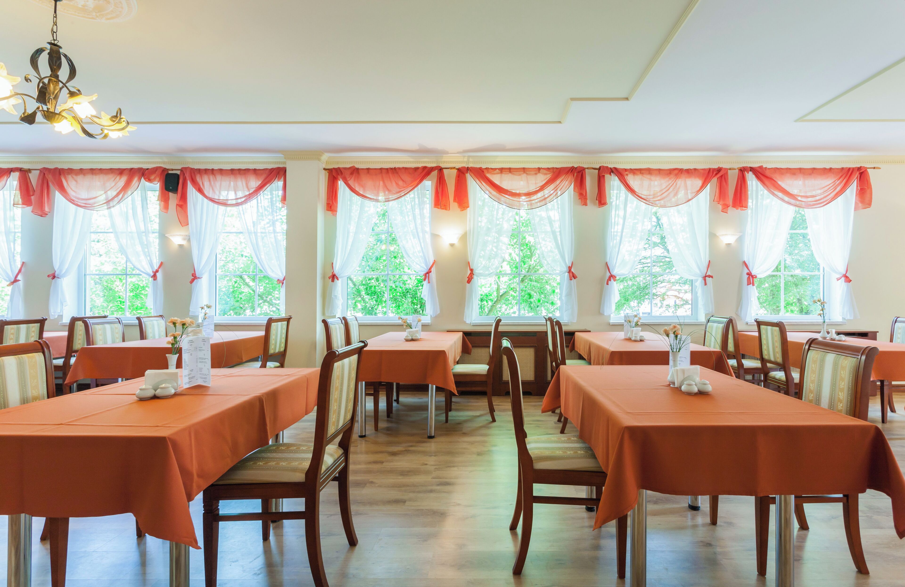 A dining area with tables set for service, chairs, and a chandelier.