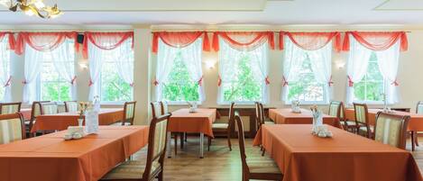 A dining area with tables set for service, chairs, and a chandelier.