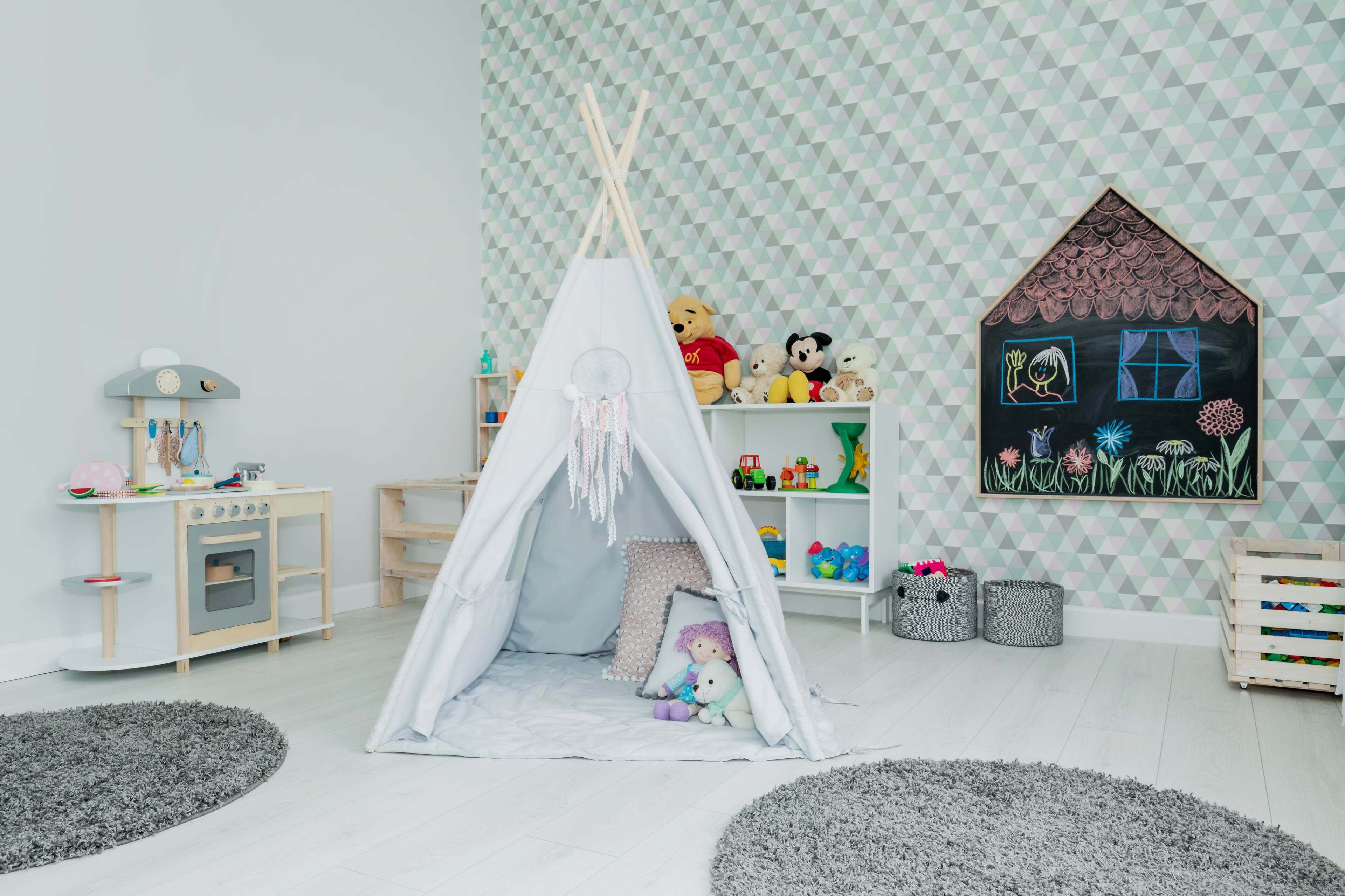 A playroom with a teepee, toys, a shelf with stuffed animals, and a wall painting.