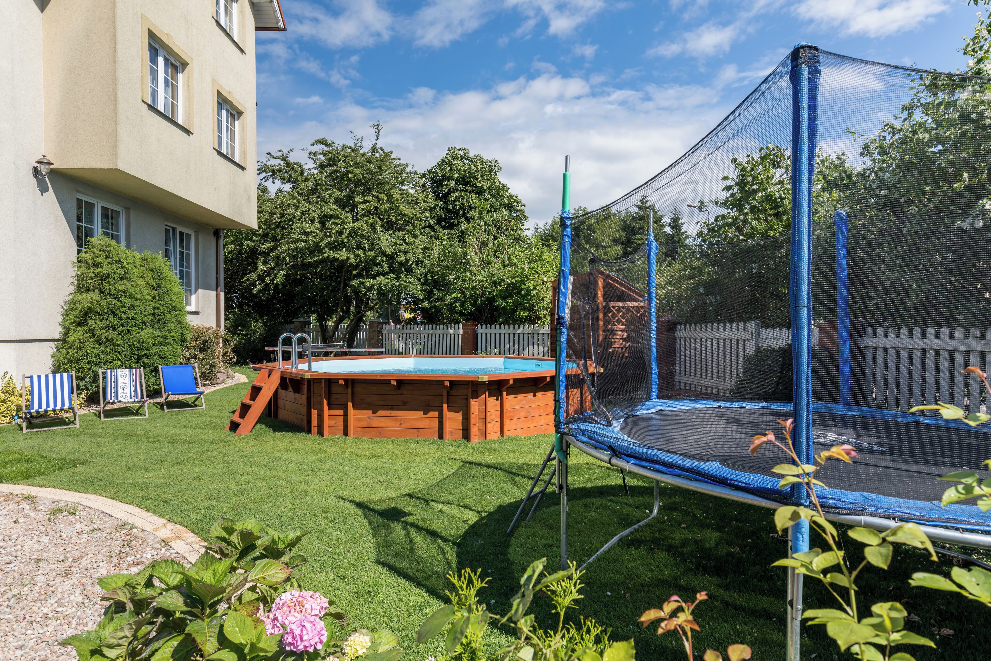 A backyard with a trampoline, a wooden deck, and a swimming pool.