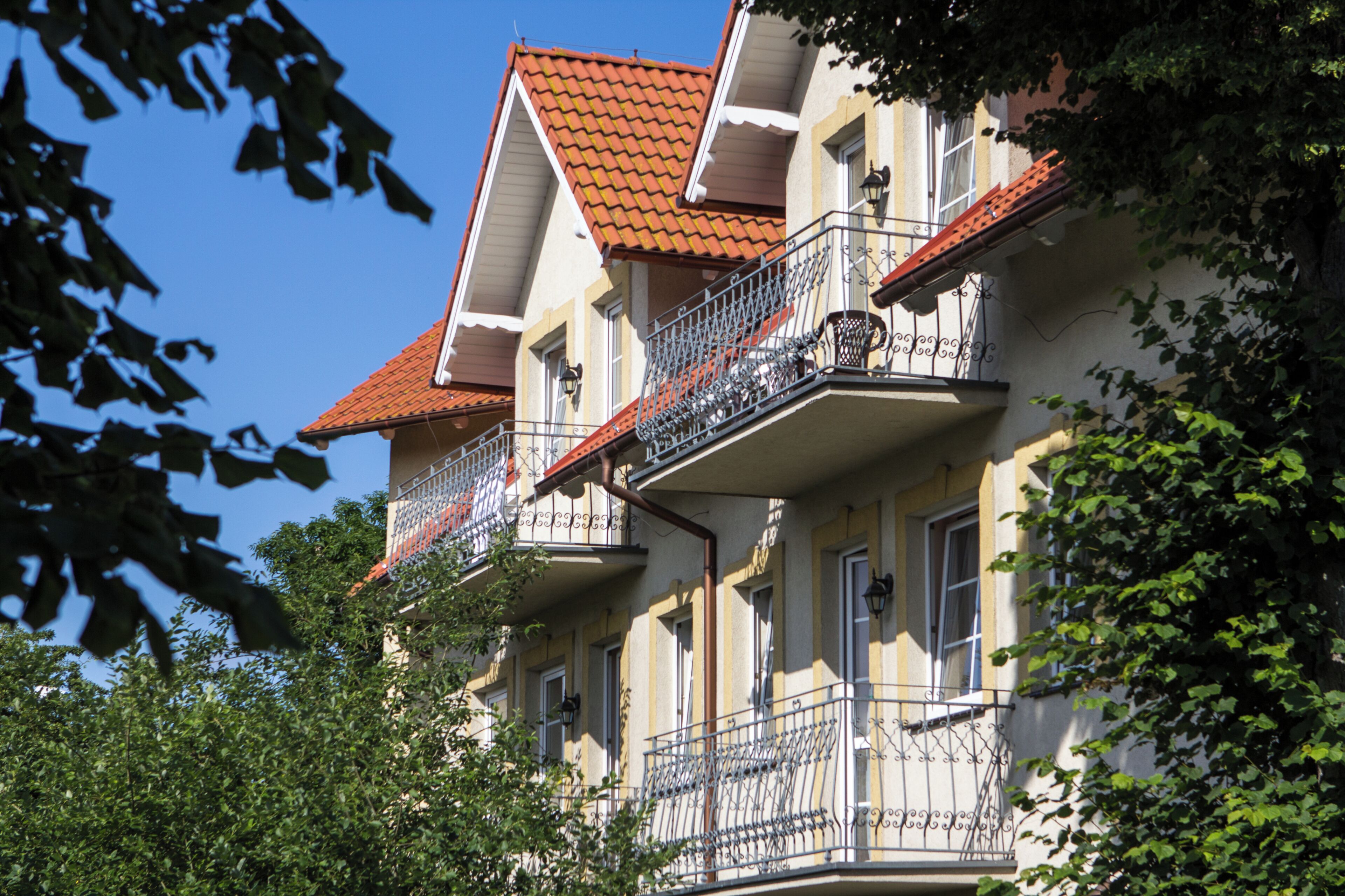 A multi-story building with balconies, a red-tiled roof, and a clear blue sky.