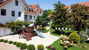 Une cour comprenant un espace de jeux pour enfants, une petite piscine et un coin salon avec des tables et des chaises.