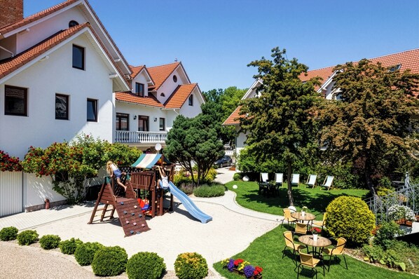Un patio con un parque infantil, una piscina pequeña y una zona de estar con mesas y sillas.