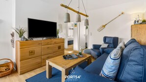 Un salon moderne avec un téléviseur, des meubles en bois, un canapé bleu et des lampes suspendues.