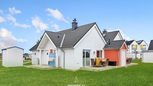 Un quartier résidentiel avec des maisons blanches, un garage et une terrasse aménagée avec du mobilier d’extérieur.