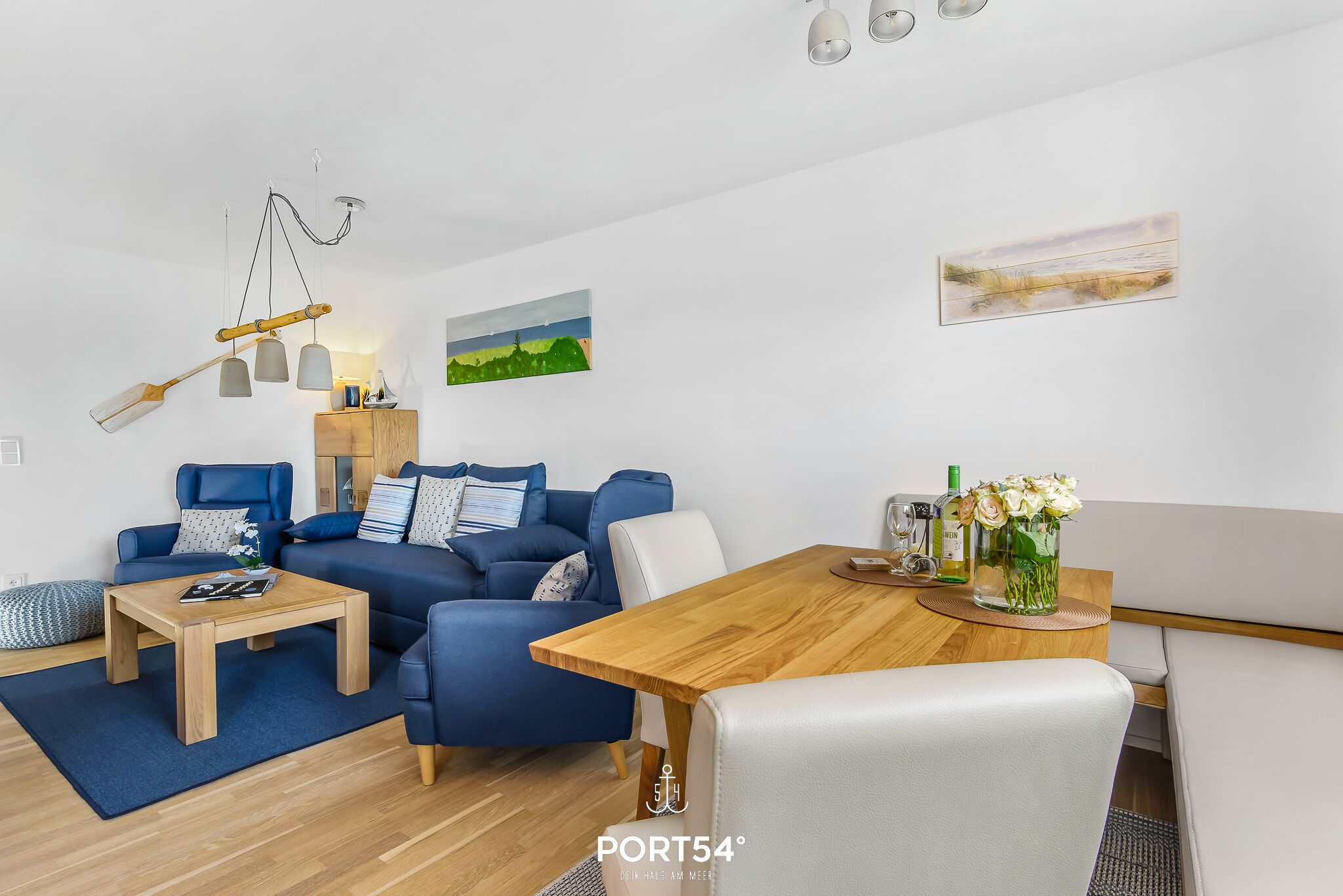 A modern living room with a blue sofa, wooden coffee table, and a dining area with a wooden table and white chairs.