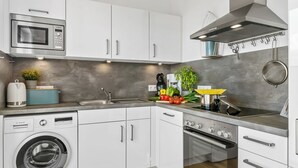Une cuisine moderne avec des meubles blancs, un lave-linge Bosch, un four à micro-ondes, une cuisinière et un évier.