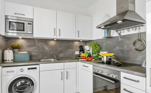 A modern kitchen with white cabinets, a Bosch washing machine, a microwave, a stove, and a sink.