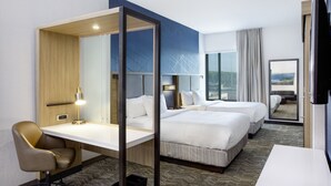 Ein Hotelzimmer mit Schreibtisch, zwei Betten, einem Sessel, einem Fernseher und einem großen Fenster mit Blick.