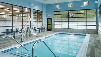 An indoor swimming pool with clear markings, a tiled floor, and a view of trees through large windows.