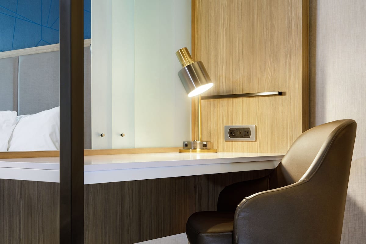 A modern hotel room with a wooden accent wall, a desk with a lamp, and a leather chair.